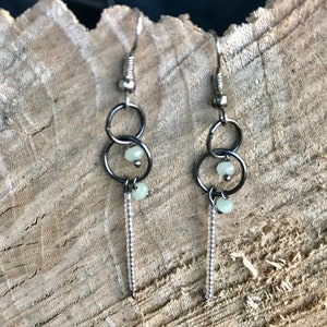 May include: A pair of silver dangle earrings with two small green beads and a long chain of silver beads.
