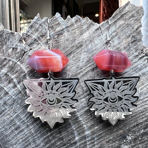May include: A pair of silver earrings with a red agate stone and a silver triangle pendant with an eye and sun design.