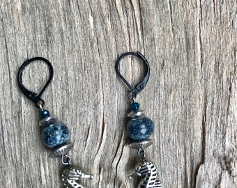 May include: A pair of silver seahorse earrings with blue and white speckled beads and black hooks.