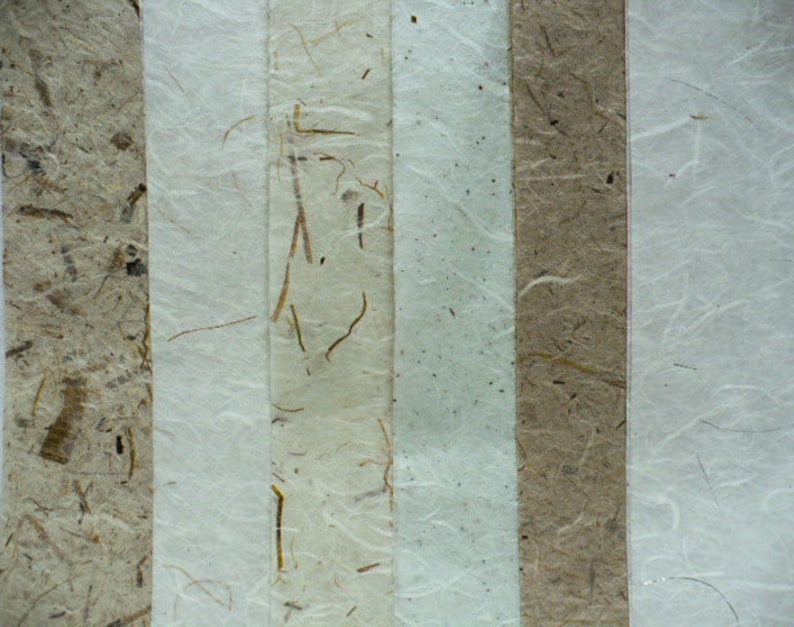 Puede incluir: Primer plano de cinco tiras verticales de papel hecho a mano con diferentes texturas y colores. El papel es blanco, marr&oacute;n claro y beige con fibras y motas visibles.