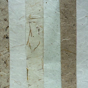 May include: Close-up of five vertical strips of handmade paper with different textures and colors. The paper is white, light brown, and beige with visible fibers and flecks.