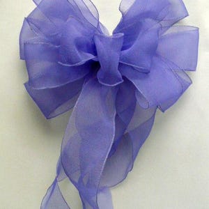 May include: A large, decorative bow made of sheer, lavender-colored ribbon. The bow features multiple loops and long, flowing tails. The ribbon has a subtle sheen, and the edges are finished with a delicate stitching.