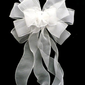 May include: A large, decorative bow crafted from sheer, translucent white organza ribbon. The bow features multiple layered loops and two long, flowing ribbon tails that cascade downward, creating a soft, airy, and voluminous appearance.