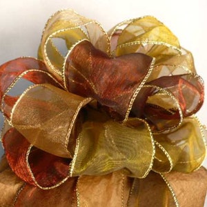 May include: A large, decorative bow made of gold and brown sheer ribbon with gold wired edges. The bow is tied on a brown paper package.