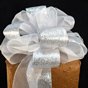 May include: A silver and white gift bow with a sparkly finish. The bow is tied around a brown package.