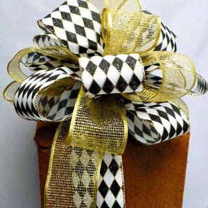 May include: A decorative bow crafted from two distinct ribbons: one featuring a black and white diamond harlequin pattern and the other a sheer, metallic gold mesh. The bow has multiple loops and two long, trailing ribbon tails.