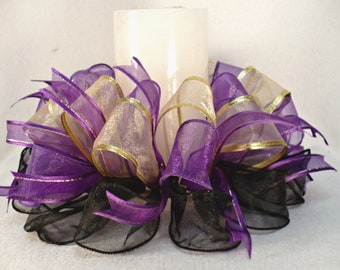 May include: A purple, gold, and black ribbon centerpiece with a white candle in the center.