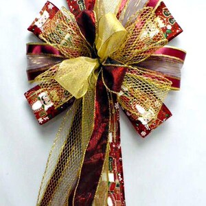 May include: A decorative bow featuring a red ribbon with a nutcracker print, layered with gold metallic mesh ribbon and solid deep red satin ribbon. The bow has multiple loops and long trailing tails, showcasing a festive pattern of nutcrackers.