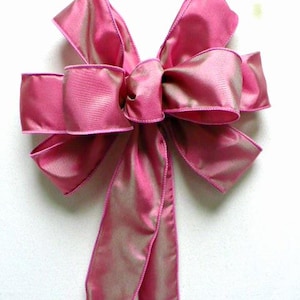 May include: A large pink satin bow with a wired edge. The bow is tied with two long tails.