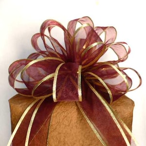 May include: A burgundy sheer ribbon bow with gold trim. The bow is tied on a brown package.