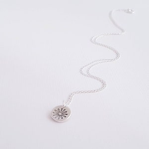 May include: A silver chain necklace with a small, round pendant featuring a delicate daisy design.
