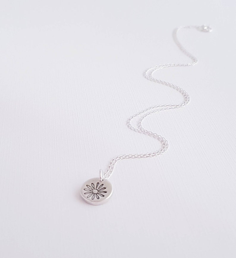 May include: A silver chain necklace with a small, round pendant featuring a delicate daisy design.