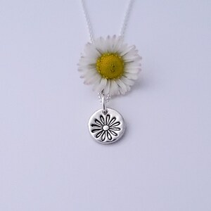 May include: A silver necklace with a delicate daisy charm. The charm is a round disc with a raised daisy design.