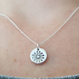 May include: A silver chain necklace with a silver pendant featuring a daisy design.