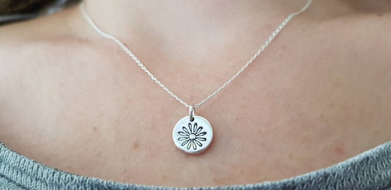 May include: A silver chain necklace with a silver pendant featuring a daisy design.