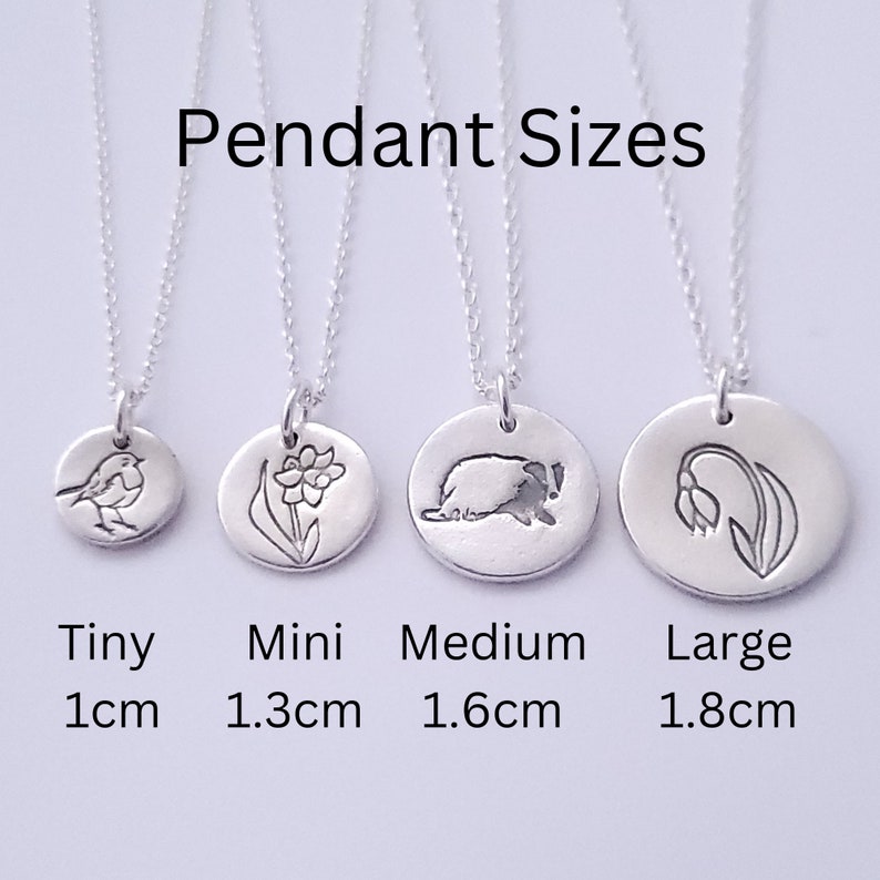 May include: Four silver pendant necklaces with different designs and sizes. The pendants are 1 cm, 1.3 cm, 1.6 cm, and 1.8 cm in diameter. The designs include a robin, a daffodil, a hedgehog, and a lily of the valley.