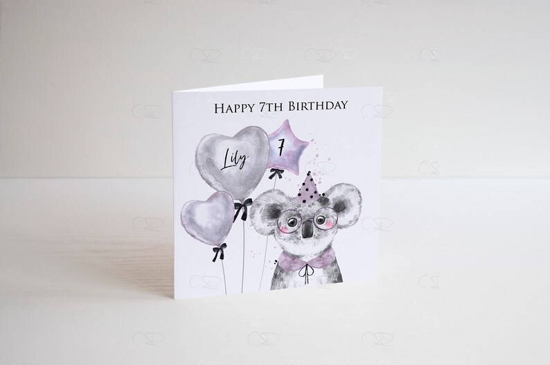 May include: A white card with the text "Happy 7th Birthday" and the name "Lily" written on a heart-shaped balloon. A koala wearing glasses and a party hat is holding a star-shaped balloon with the number "7" on it.