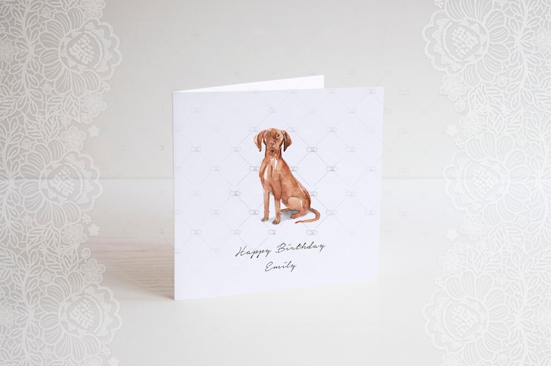 Pode incluir: Um cart&atilde;o branco com uma ilustra&ccedil;&atilde;o em aquarela de um c&atilde;o marrom sentado. O cart&atilde;o tem o texto "Happy Birthday Emily" impresso nele.