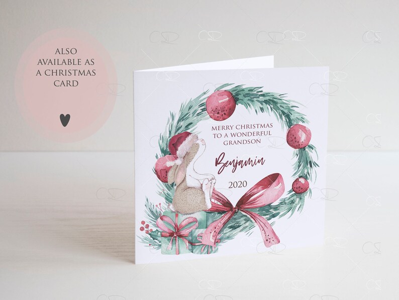 May include: A Christmas card featuring a watercolor illustration of a bunny wearing a Santa hat, sitting on a gift box with a red bow. The bunny is surrounded by a green wreath with red berries and a pink bow. The text "Merry Christmas to a wonderful Grandson Benjamin 2020" is written on the card.