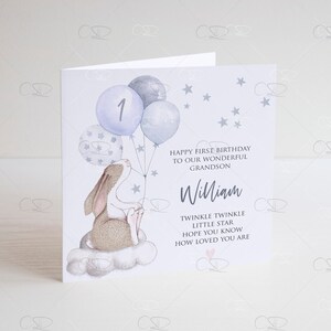 May include: A light blue card with a white background. The card features a cartoon bunny holding blue balloons with white stars. The balloons have the number "1" on one of them. The card has the text "Happy First Birthday to our wonderful Grandson William. Twinkle Twinkle Little Star Hope you know how loved you are."