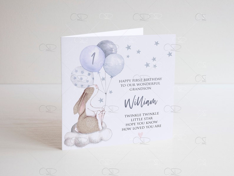 May include: A light blue card with a white background. The card features a cartoon bunny holding blue balloons with white stars. The balloons have the number "1" on one of them. The card has the text "Happy First Birthday to our wonderful Grandson William. Twinkle Twinkle Little Star Hope you know how loved you are."