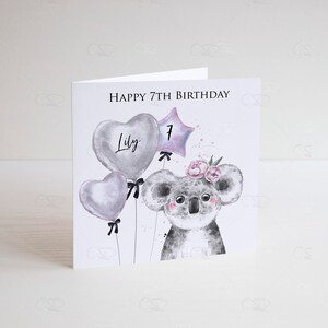 May include: A white card with the text "Happy 7th Birthday" and the name "Lily" written on a heart-shaped balloon. A koala with a flower crown is holding a star-shaped balloon with the number "7" on it. The background is white.