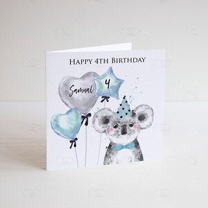 May include: A birthday card featuring a cute koala wearing a party hat and holding balloons. The balloons are blue, gray, and star-shaped with the number "4" and the name "Samuel" written on them. The card says "Happy 4th Birthday".