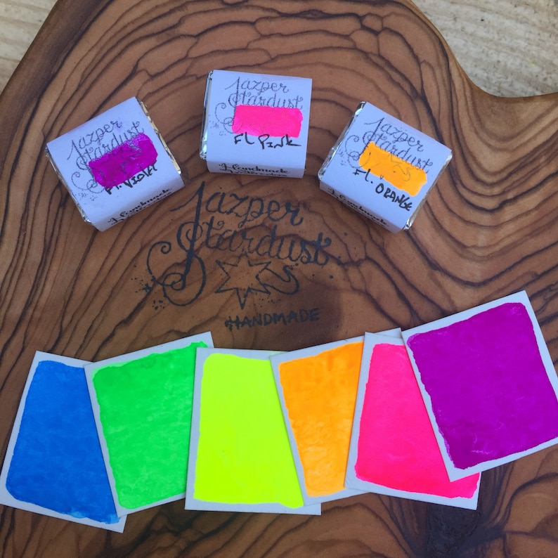 May include: Six small squares of neon colored paint samples. The colors are blue, green, yellow, orange, pink, and purple. The paint is labeled "Jazper Stardust" and "Handmade".