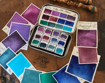 May include: A set of 16 watercolor paints in a metal tin with a label that reads "Into the Mystic." The paint colors are a mix of blues, greens, and purples. The paint pans are arranged in a grid pattern. A sample of the paint color "Monastral Violet" is shown on a separate card.