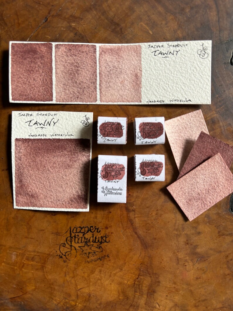 May include: Three watercolor paint swatches in shades of brown, labeled "Jasper Stardust Tawny" and "Handmade Watercolor".  There are also four small watercolor pans labeled "Jasper Stardust Tawny" and "Handmade Watercolor".