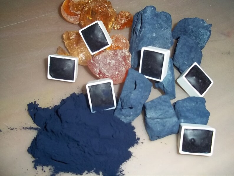 May include: A collection of blue watercolor paint pans, a pile of blue pigment, and a pile of orange and brown resin.