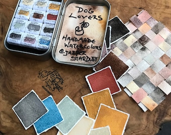 May include: A tin of handmade watercolor paints labeled "Dog Lovers" with various color swatches. The tin includes individual paint squares with names like "Feal" and "G.O." A woven swatch of various colors is also present.