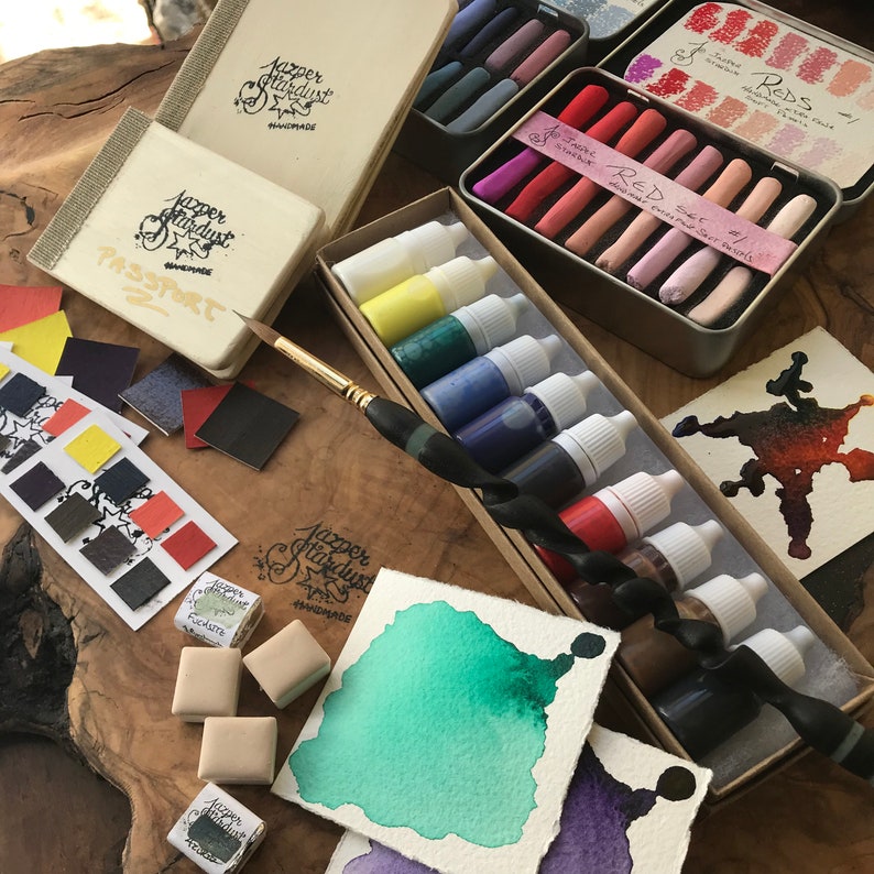 May include: A set of watercolor paints in a variety of colors, including red, green, blue, and black. The paints are in small bottles and are arranged in a box. There are also some watercolor pencils and a paintbrush in the image.