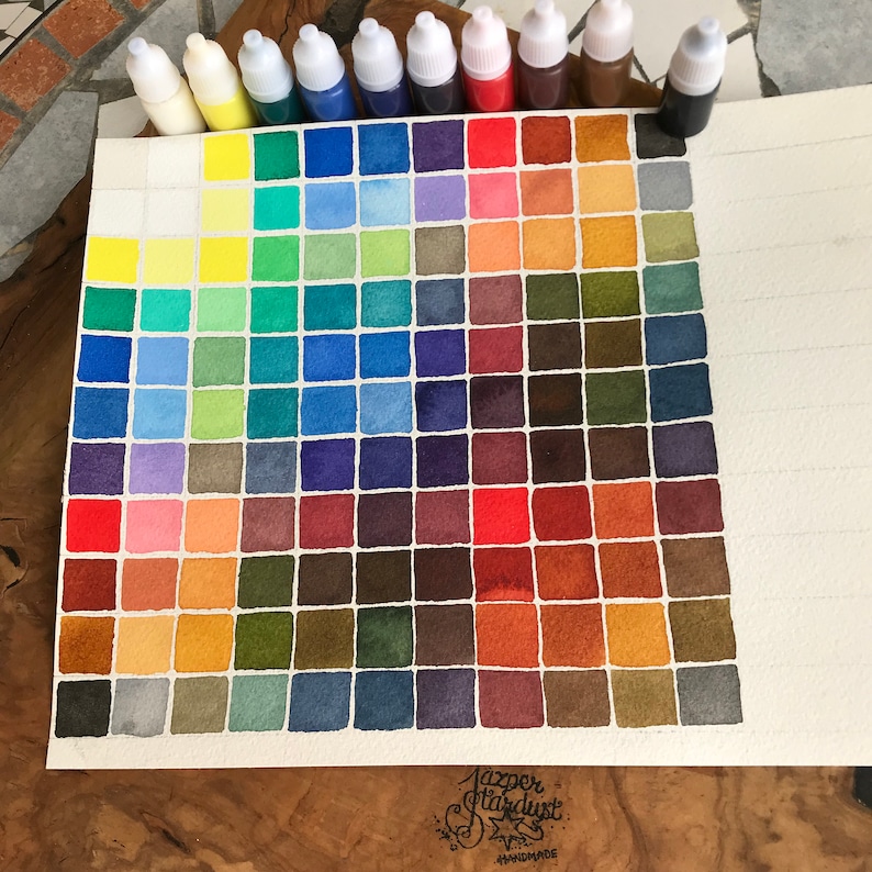 May include: A watercolor paint chart with 64 color swatches arranged in a triangular pattern. The colors range from yellow to red to blue to green to brown. The chart is labeled "Jazzer Stardust Handmade".