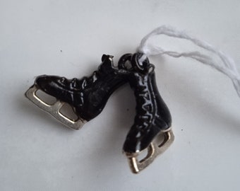 May include: A pair of black ice skate charms with silver blades. The charms are attached to a white string.
