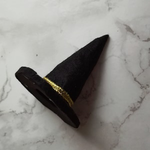 May include: A small black witch's hat with a gold band around the base. The hat is made of a felt-like material and has a pointed crown. This decorative hat is perfect for Halloween or themed events.