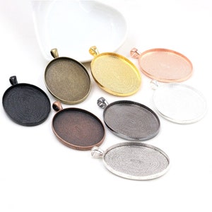 May include: Assortment of seven oval-shaped pendant trays in various metallic finishes, including silver, gold, black, copper, and rose gold. Each tray has a textured surface and a loop at the top for attaching a pendant.