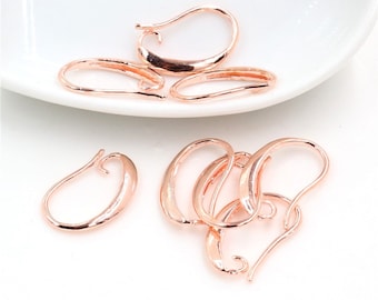 May include: Rose gold-colored earring hooks in various shapes and sizes are displayed on a white surface. The hooks have a curved design, with some featuring a loop at the end for attaching earrings. The metal has a shiny finish.