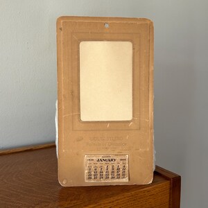 May include: Vintage 1936 calendar with a rectangular photo frame. The calendar features the month of January, with the text "WOLTZ STUDIO Portraits of Destination" printed above the calendar. The calendar is a light brown color.