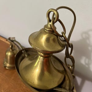 May include: Close-up of a vintage brass chandelier fixture. The fixture features a decorative bowl, a central stem, and a chain for hanging. The brass has a warm, aged patina, suggesting its antique nature. The design is ornate and detailed.
