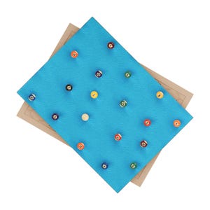 Op de afbeelding: Een rechthoekig bord bedekt met felblauw gestructureerd materiaal met een raster van vijftien kleurrijke genummerde biljartballen ingebed in het oppervlak, geplaatst over een groter beige rechthoekig bord met gegraveerde geometrische lijnpatronen.