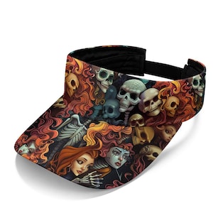 May include: A sun visor featuring an all-over print of stylized human skulls and female faces with flowing orange and red hair. The design includes skeletal elements and dark, intricate details set against a black background with an adjustable strap.