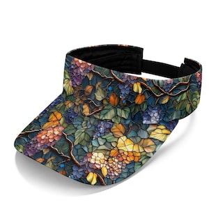 May include: A sun visor featuring a stained glass style pattern of purple grapes, brown vines, and green leaves. The visor has a curved brim and a black adjustable strap at the back, showcasing a vibrant, multi-colored mosaic design throughout.