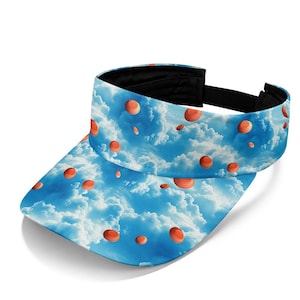 May include: A sun visor featuring a sky blue background with white clouds and a repeating pattern of small orange circular clay targets. The visor has a curved brim and a black adjustable strap at the back with a black interior lining.