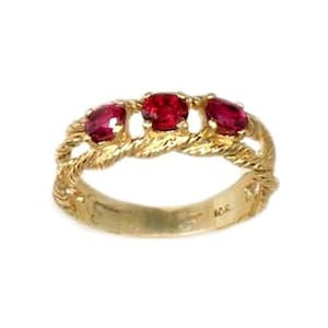 May include: A gold band ring with three red gemstones set in a twisted rope design.