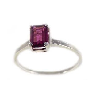 Puede incluir: Un anillo de plata con una piedra preciosa de color púrpura oscuro de corte esmeralda.