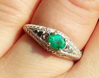May include: A silver ring with an emerald green gemstone set in a delicate filigree design.