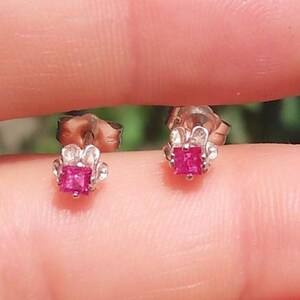 Könnte beinhalten: Ein Paar silberne Ohrstecker mit einem kleinen quadratischen rosa Edelstein in der Mitte jedes Ohrsteckers. Die Ohrstecker haben ein zartes Blumenmuster um den Edelstein herum.