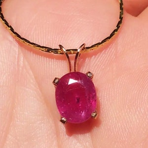 May include: A gold chain necklace with a pendant featuring a large, oval-shaped ruby gemstone set in a gold setting with small diamonds.