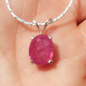 Puede incluir: Un collar de cadena de plata con un colgante de rubí ovalado rosa.